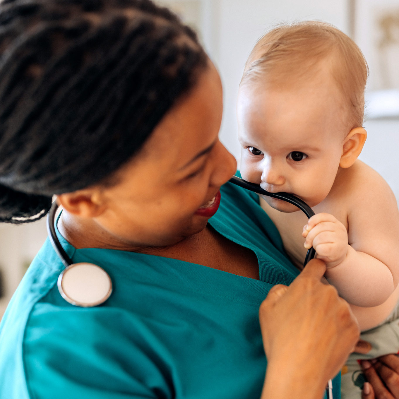 Pediatric nurse holding cute little baby boy in arms at doctor's office during checkup